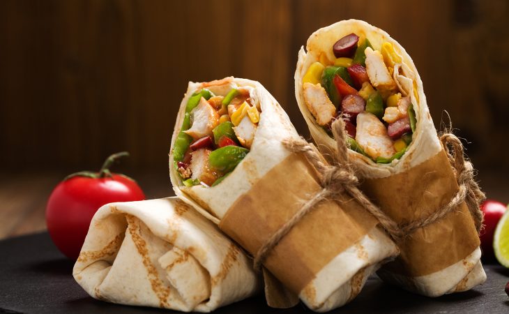 Burritos wraps with chicken, beans and vegetables on wood board
