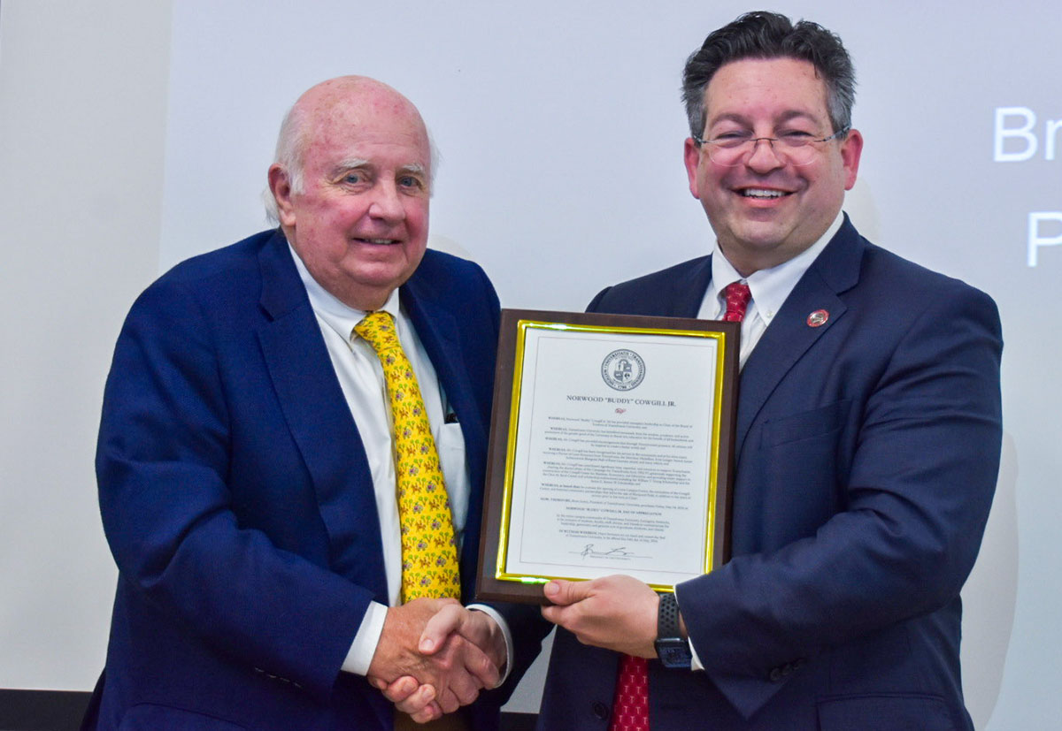 two men shaking hands, one holding a proclamation