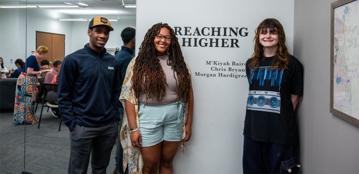 three students posing for a photo at an art exhibition