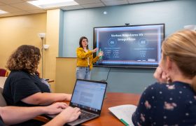 students learning from a tutor standing by a screen