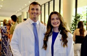 two alumni posing in their white coats