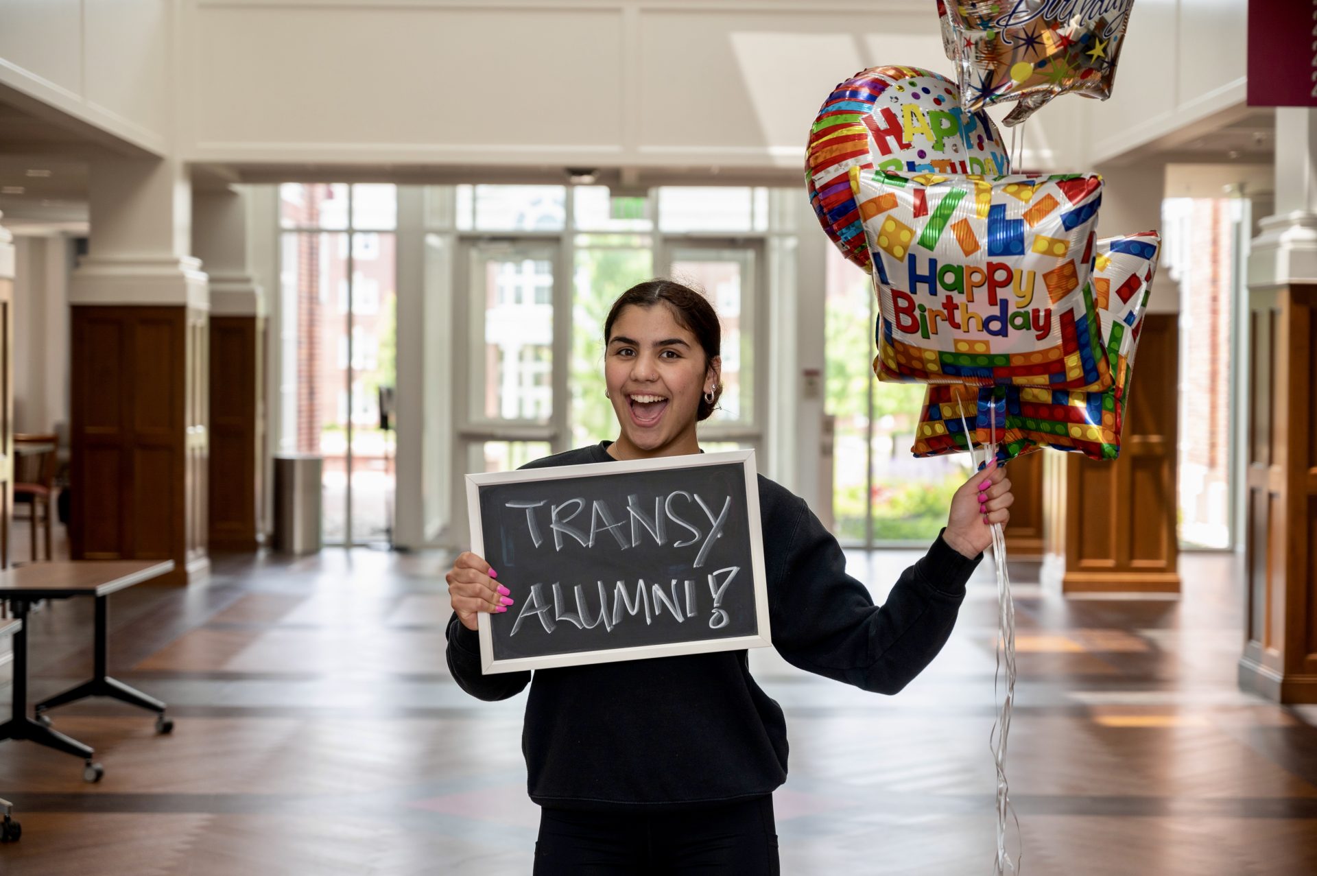 student holding a sign that says Transy Alumni and birthday balloons