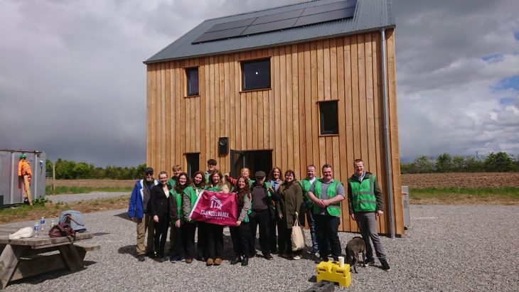 Students posing with a school flag in front of a small building