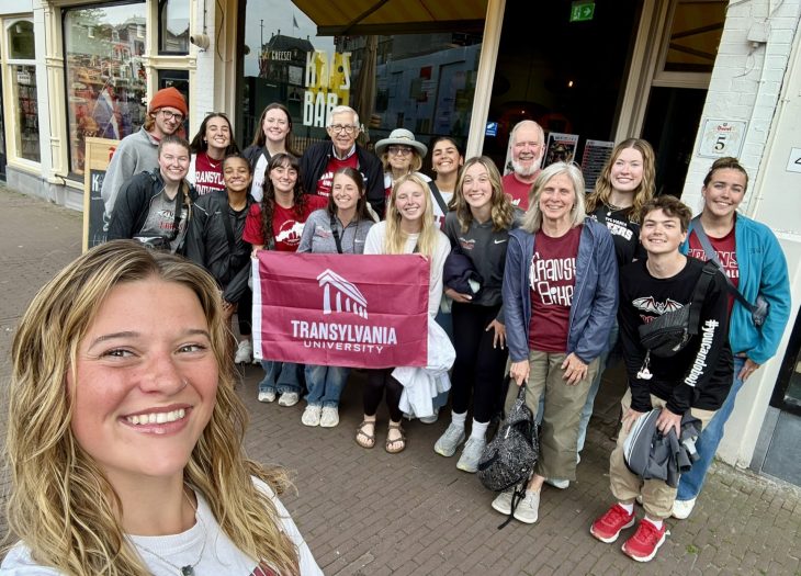 Students posing with a school flag in front of a building