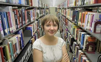 young woman standing amongst library bookshelves