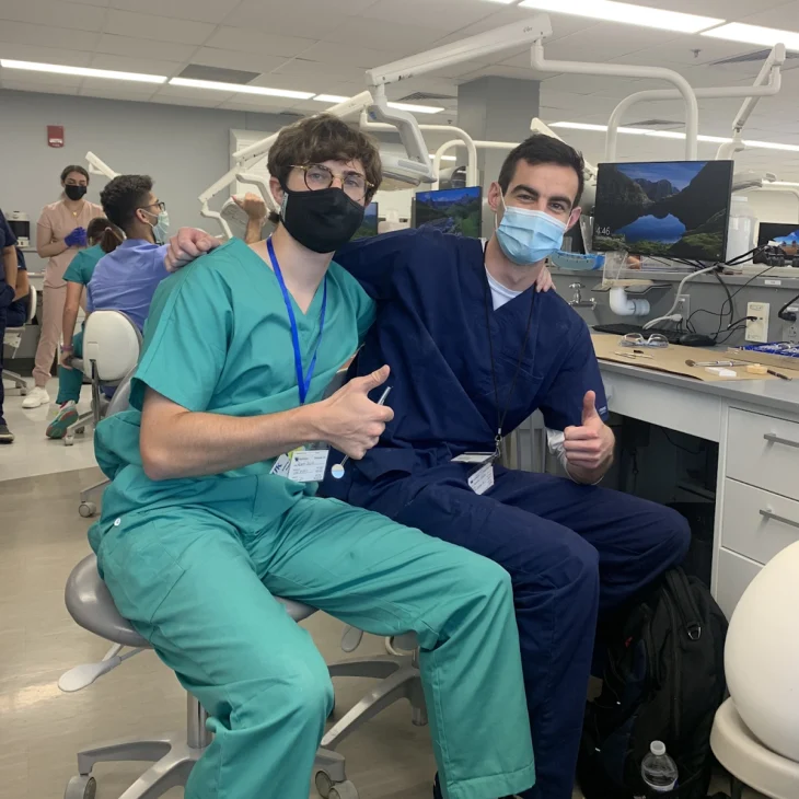 two young men in medical scrubs giving thumbs-up gesture