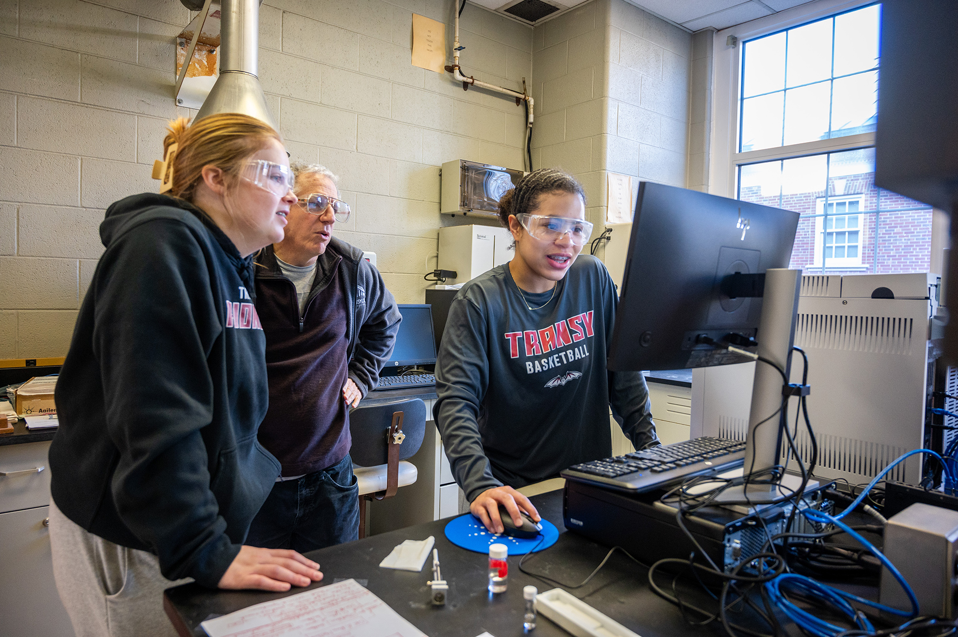 two students in lab with professor at a computer workstation