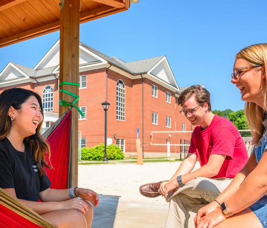 three students laughing near outdoor volleyball court