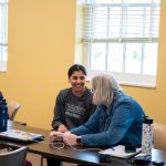 people talking while sitting at table. younger woman has smile on her face