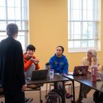 people sitting at tables in horseshoe formation. one person stands in the center