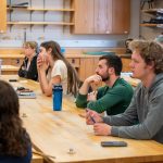 students sitting at table listening to professor speak