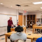 students sitting at table listening to professor speak