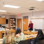 students sitting at table listening to professor speak