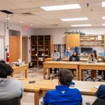 students sitting at table listening to professor speak