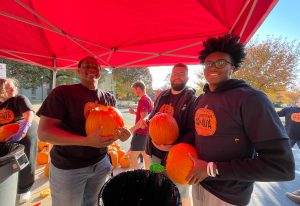 three students scooping out pumpkin guts