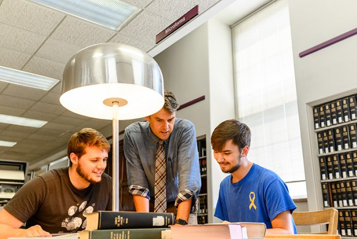 two students study in library with help from a professor