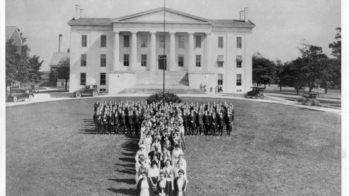 early 20th century photo of students arranged in a T formation on the lawn in front of Old Morrison. early automobiles are parked along the loop
