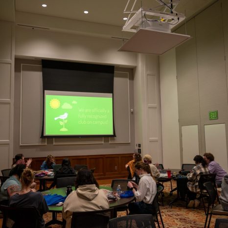 meeting guests sit at tables while presentation is projected onto a screen