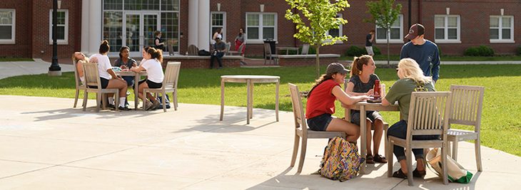 Students sitting and talking around outdoor tables on campus