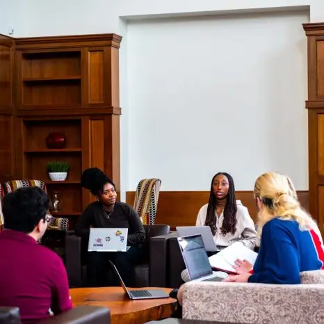 small group of students meets in room with built in natural finish wood bookshelves