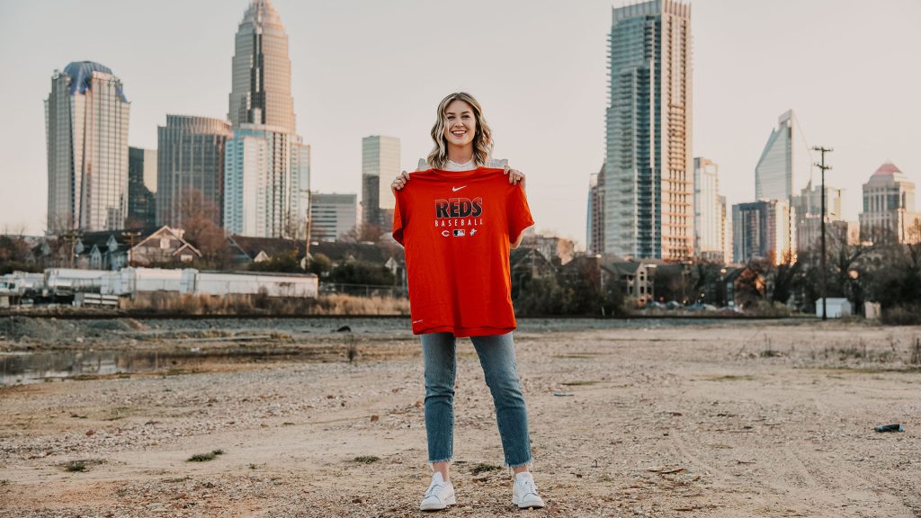 Katie Hulsman, with the Cincinnati skyline as a backdrop, holds up a Reds Baseball t-shirt