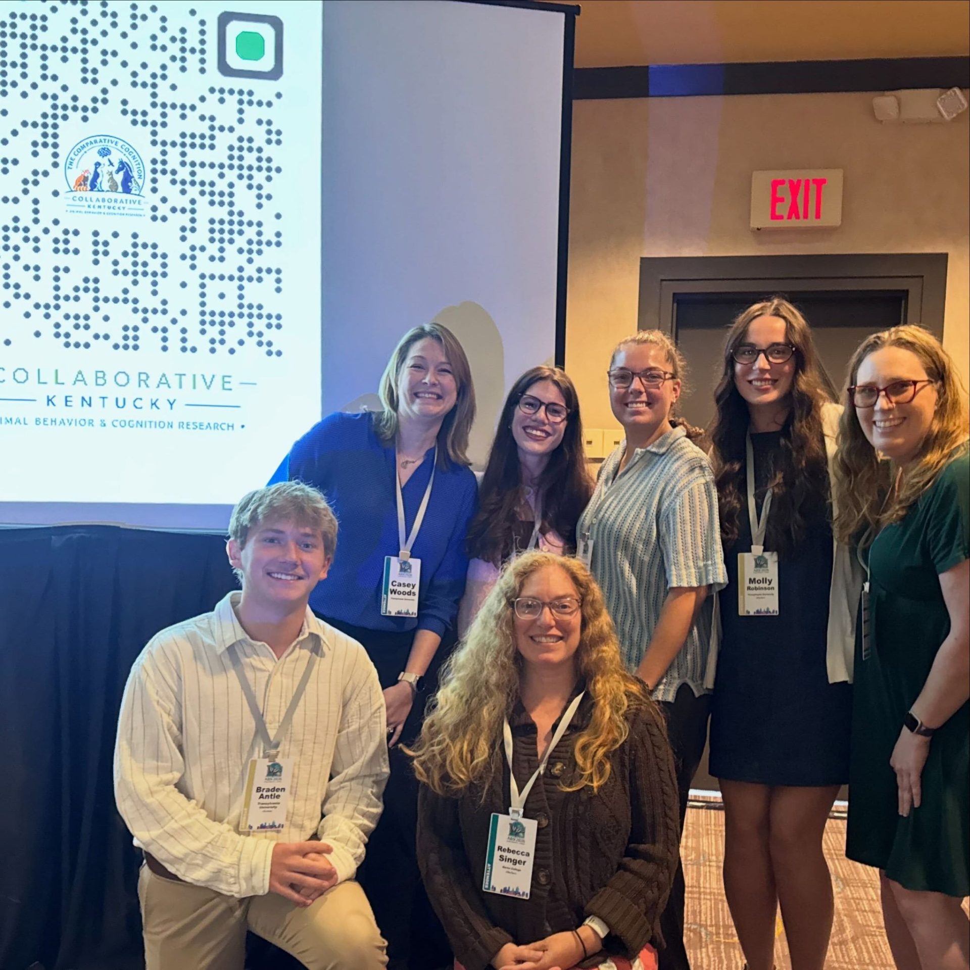 Members of the Comparative Cognition Collaborative pose together in front of a presentation screen at a conference