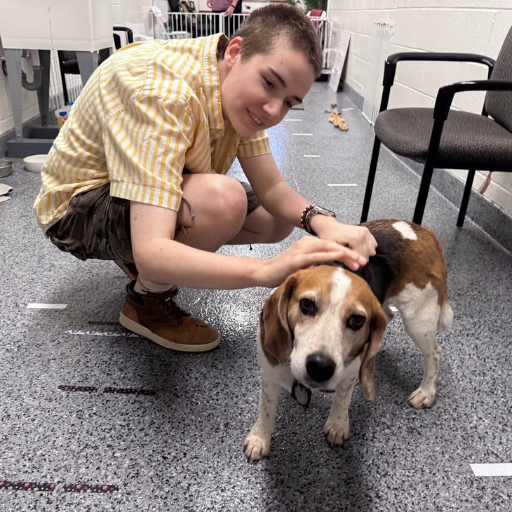 Skye crouching down to pet a small tricolor dog in a lab setting
