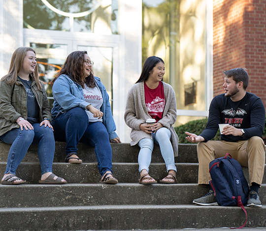 four students sitting on steps and talking