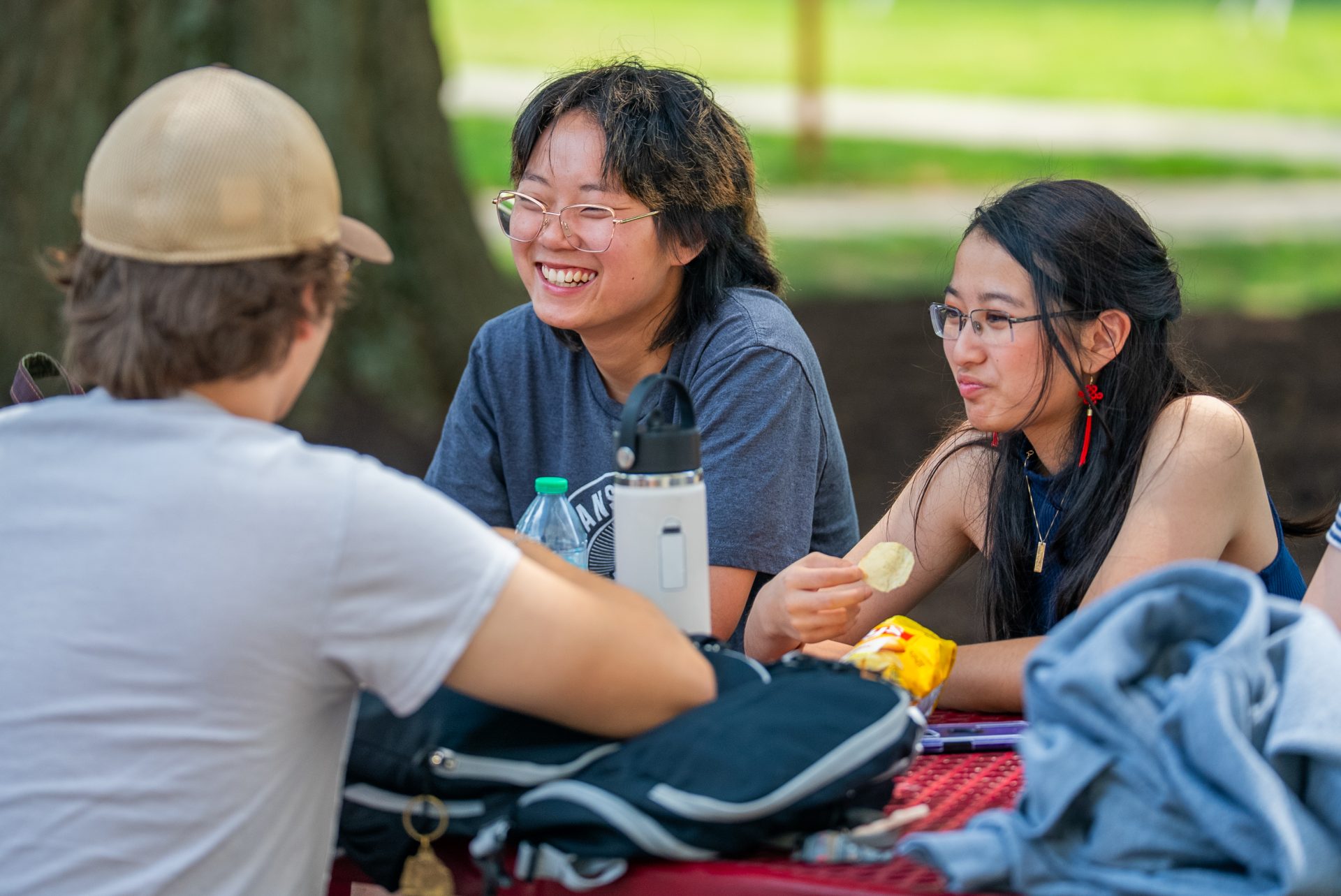 Three students laughing and talking while sitting at an outdoor table on campus