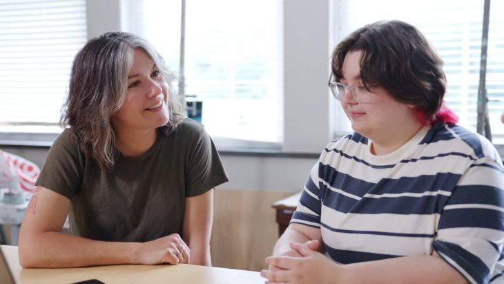 two people talking in front of a laptop